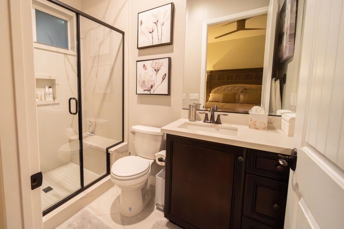 A bathroom with a vanity, mirror, toilet, and shower room.