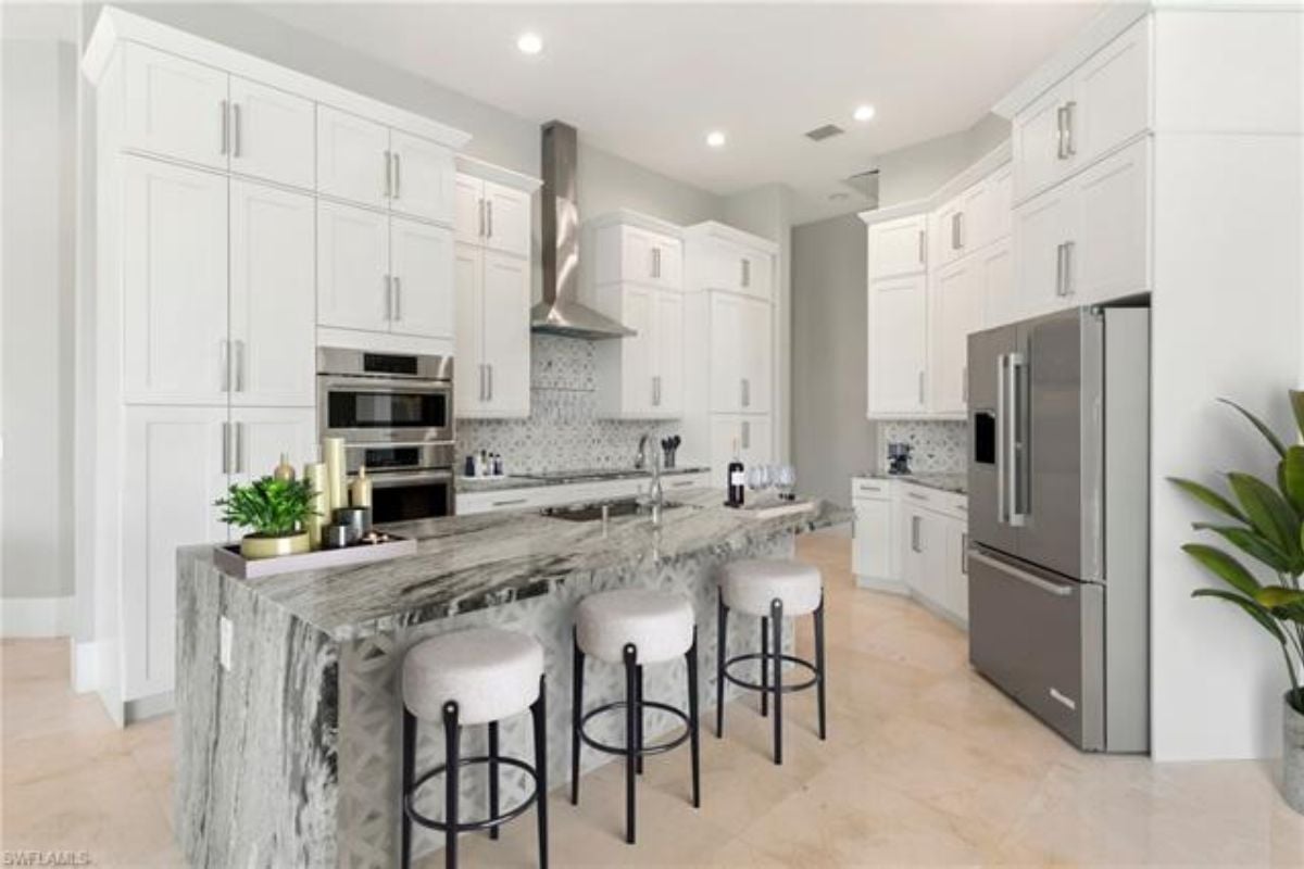A kitchen with countertops, stools, a sink, cabinets, and kitchen appliances.