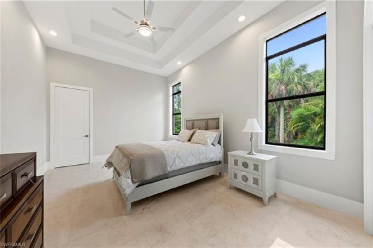 A bedroom with a bed, windows, ceiling fan and a nightstand.