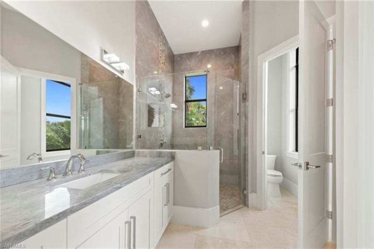 A bathroom with a vanity, cabinets, and a shower room.