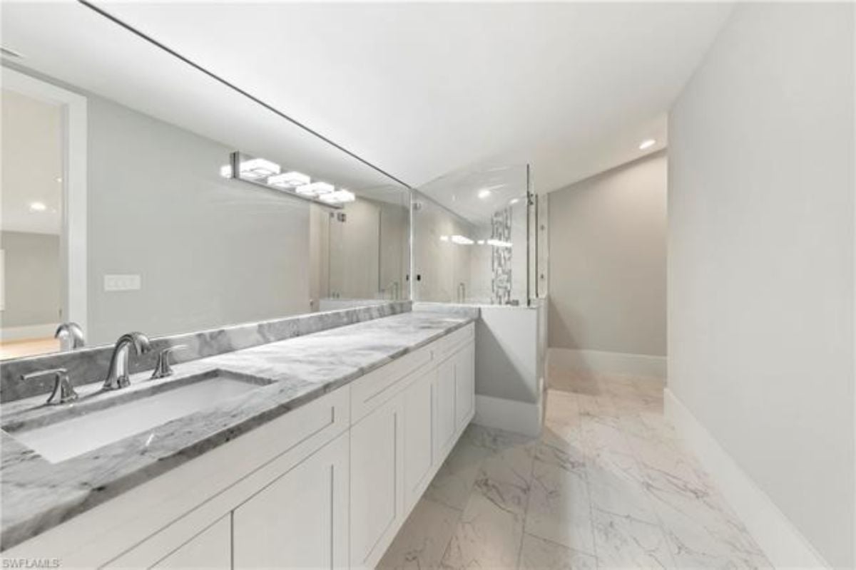 A bathroom with a vanity, cabinets, and a shower room.