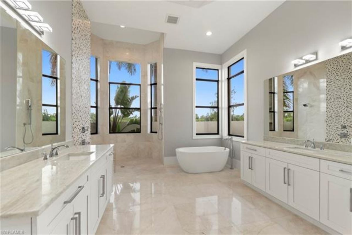 A bathroom with two vanities, mirrors, cabinets, windows, and a bathtub.