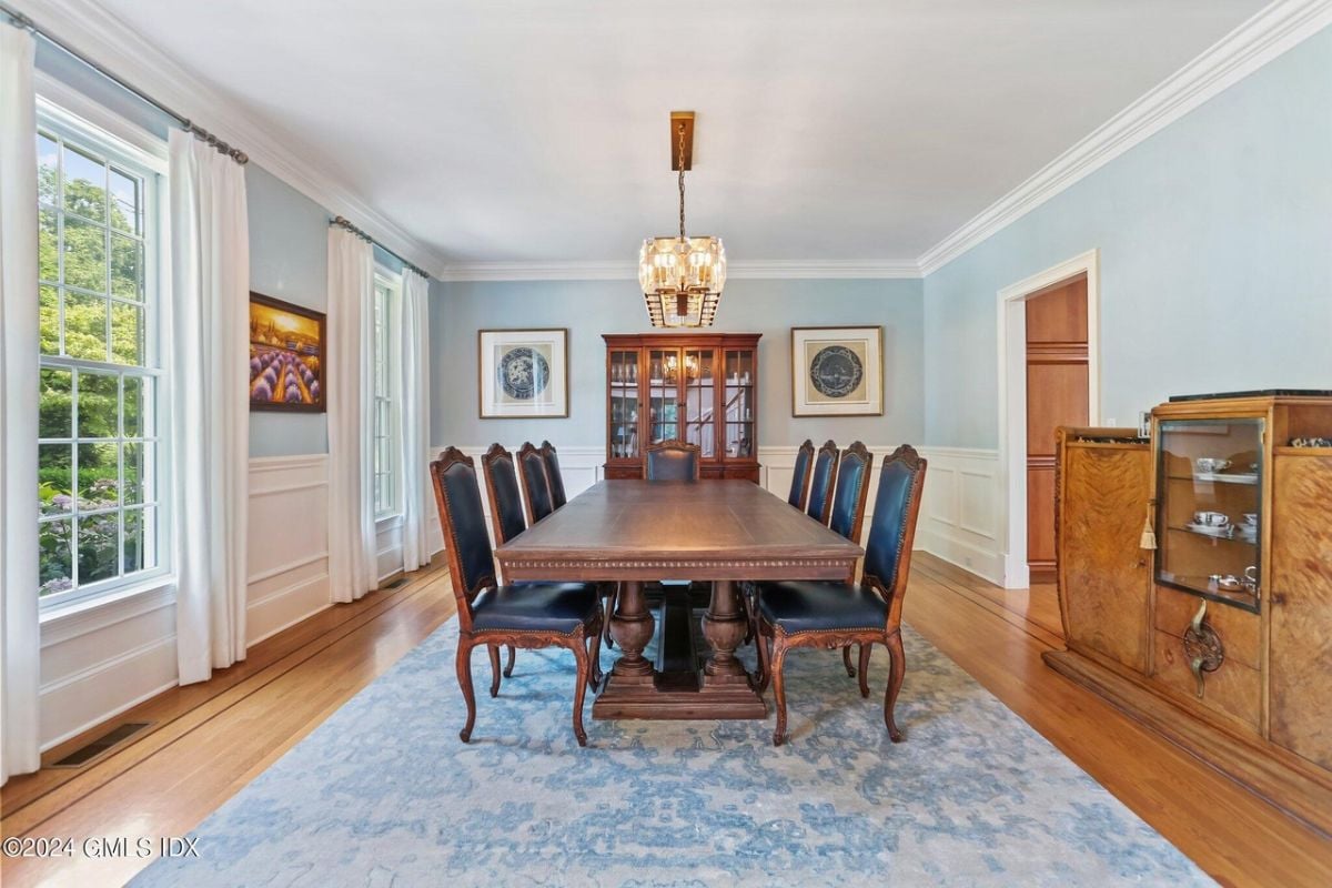 The dining room is furnished with a rug, cabinets, a chandelier, windows, and a dining table surrounded by chairs.