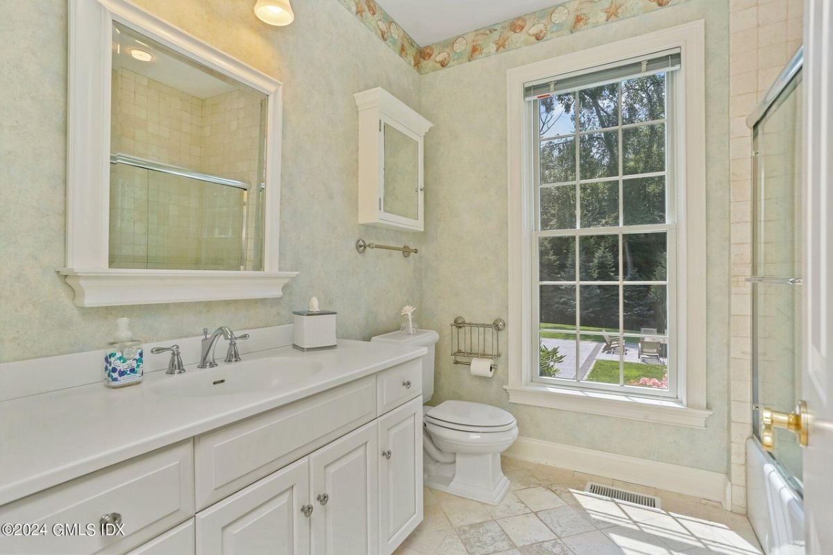 The bathroom features a vanity, cabinets, toilet, and a window.