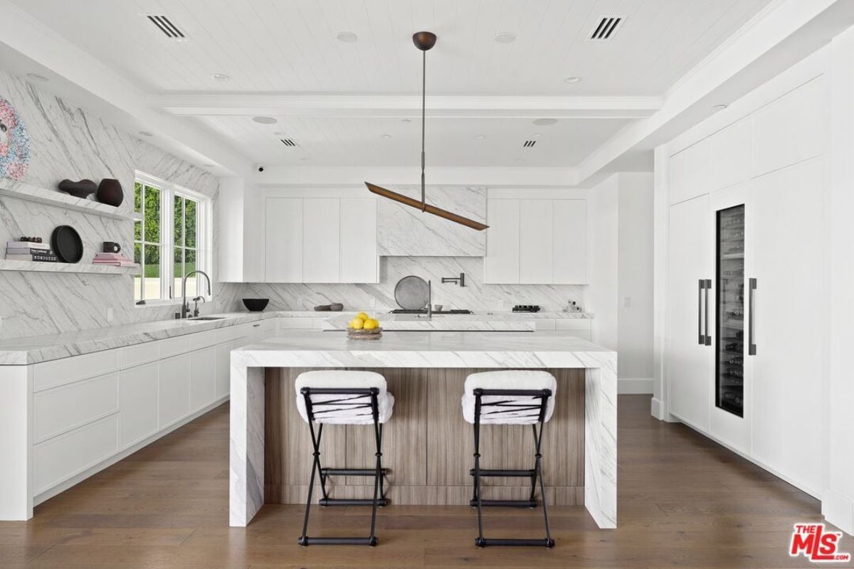 A kitchen with a center island, chairs, countertops, cabinets, and a sink.