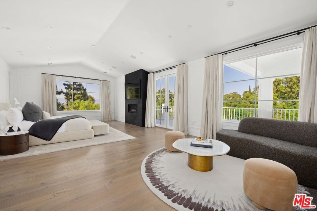 A bedroom with a bed, windows, TV, fireplace, couch, chairs, and a center table.