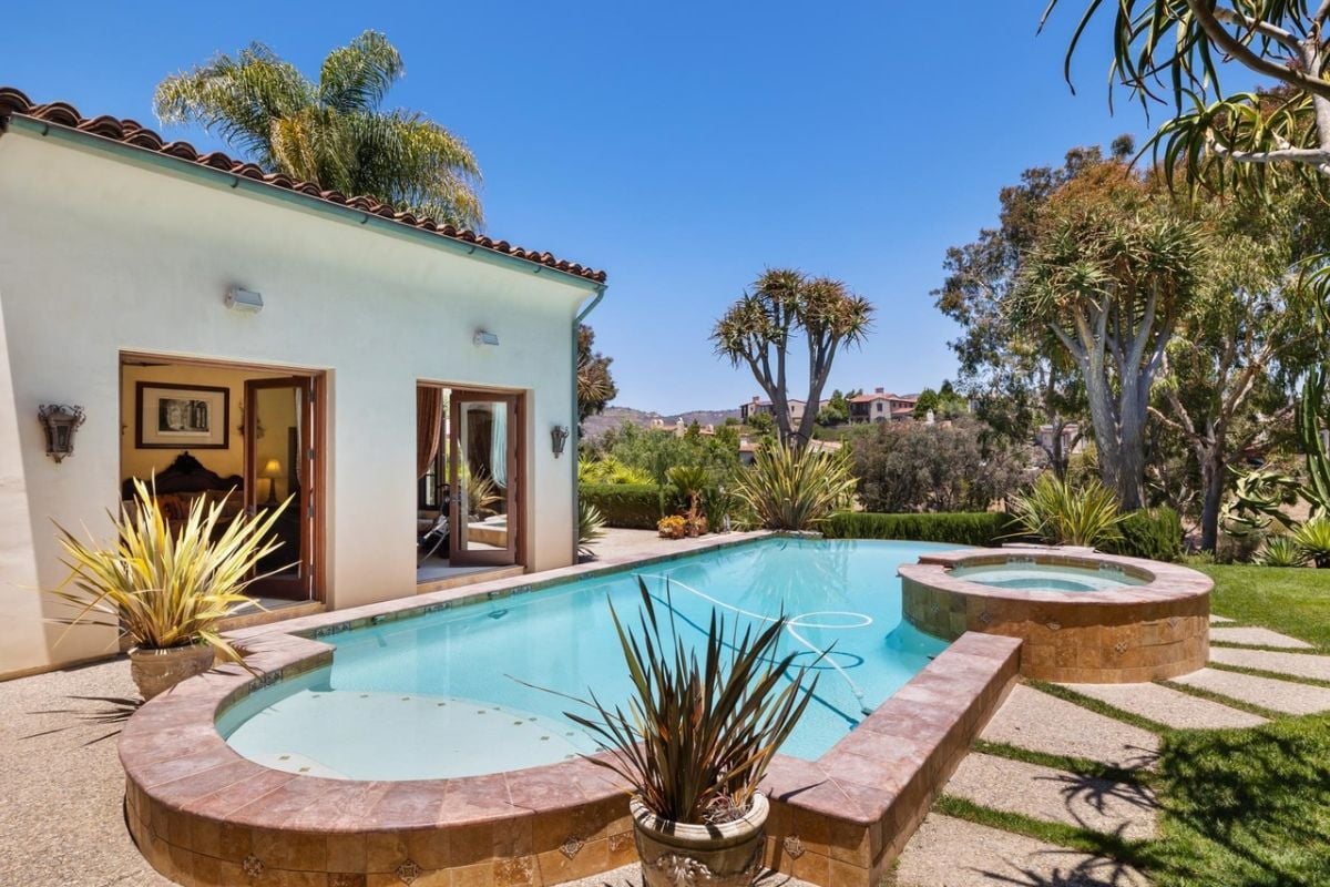 A swimming pool with a jacuzzi, surrounded by plants and trees.