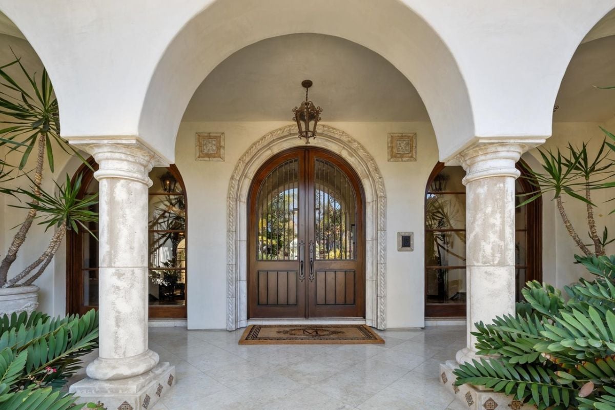 A front entry adorned with plants, a rug, and columns.