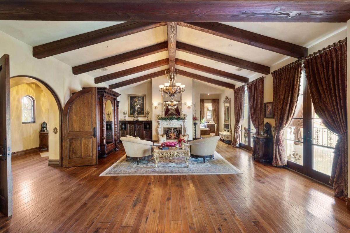 A living room with an exposed beam ceiling, fireplace, cabinets, rug, couch, and coffee table.