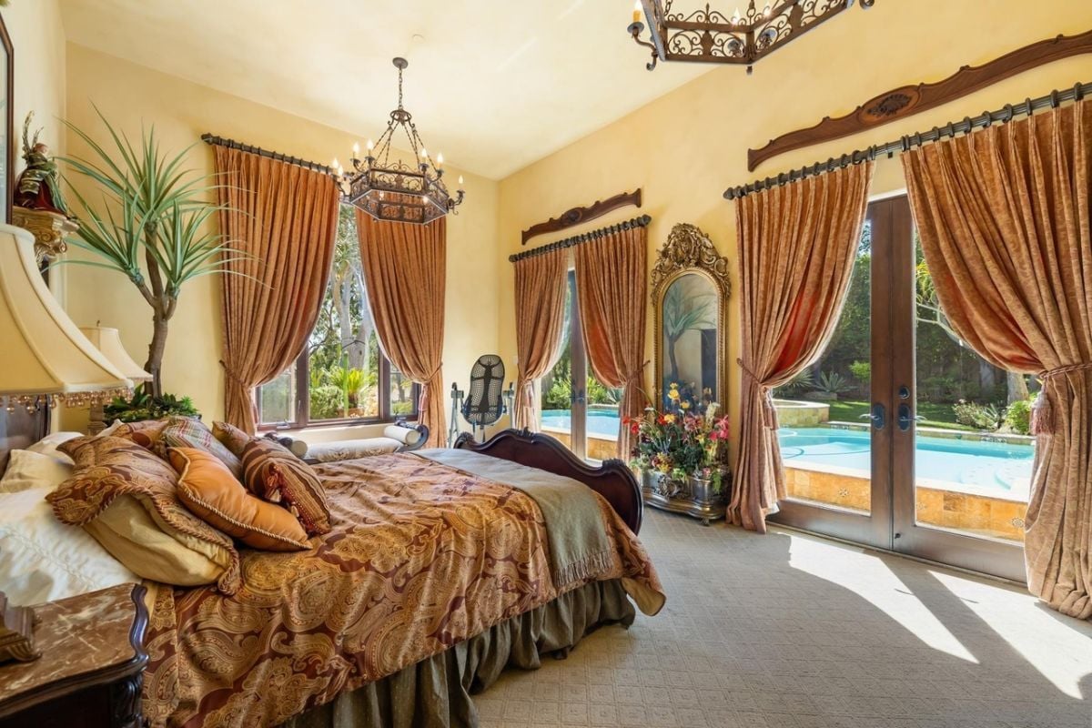 A bedroom with a bed, mirror, and windows with curtains.