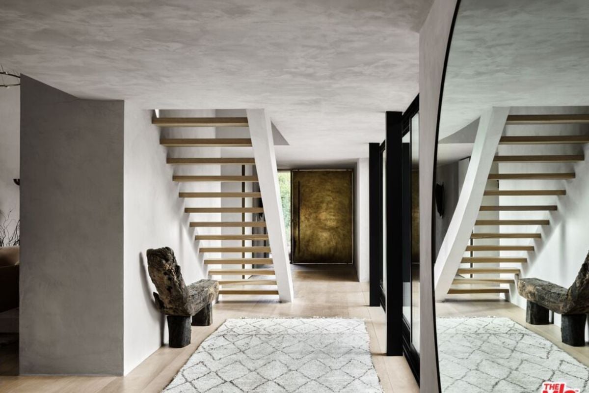 A foyer with a rug, bench, mirror, and staircase.