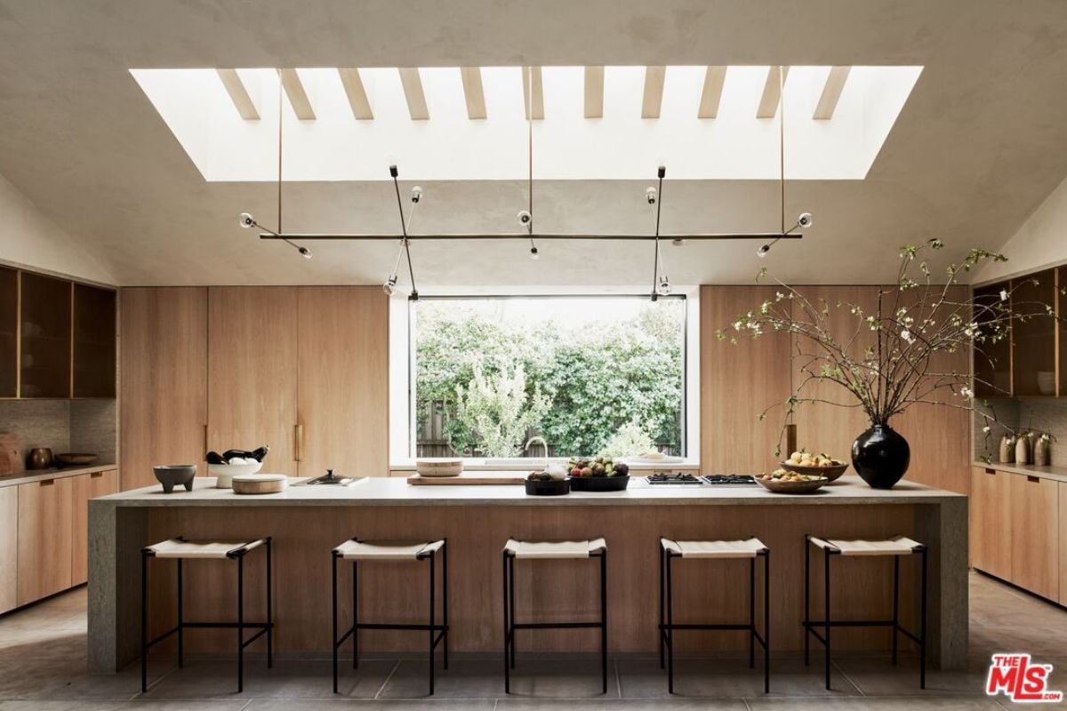 A kitchen with skylight roofing, cabinets, countertops, chairs, a window, and a sink.