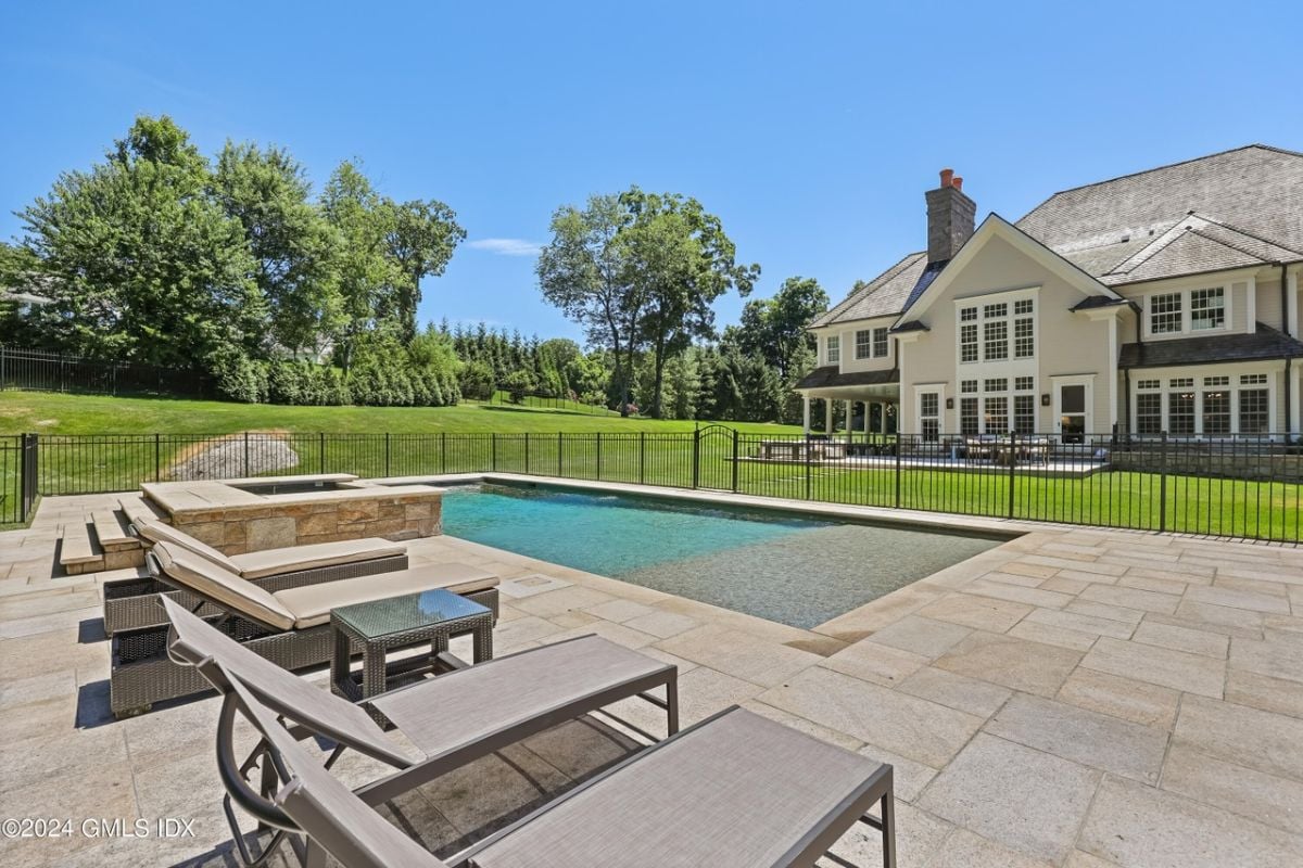 A swimming pool with a jacuzzi and chairs, surrounded by a metal fence.