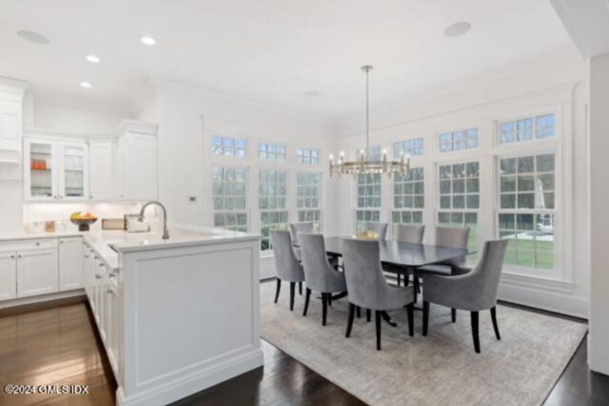 A dining area and kitchen with countertops, cabinets, sink, a chandelier, and a dining table surrounded by chairs.