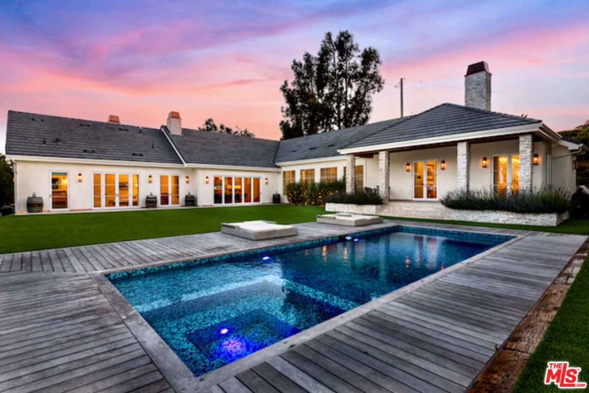 A swimming pool surrounded by a wooden deck with comfortable chairs.