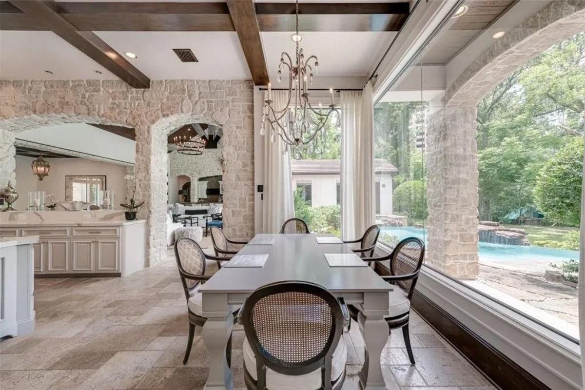 A great room with a window, chandelier, and a dining table surrounded by chairs.