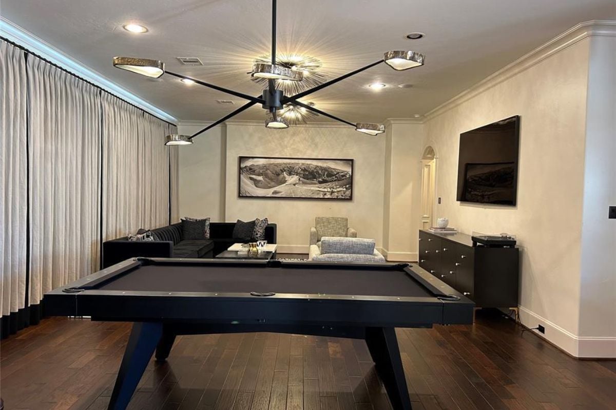 An entertainment room with a TV, cabinet, couches, painting, chandelier, and pool table.