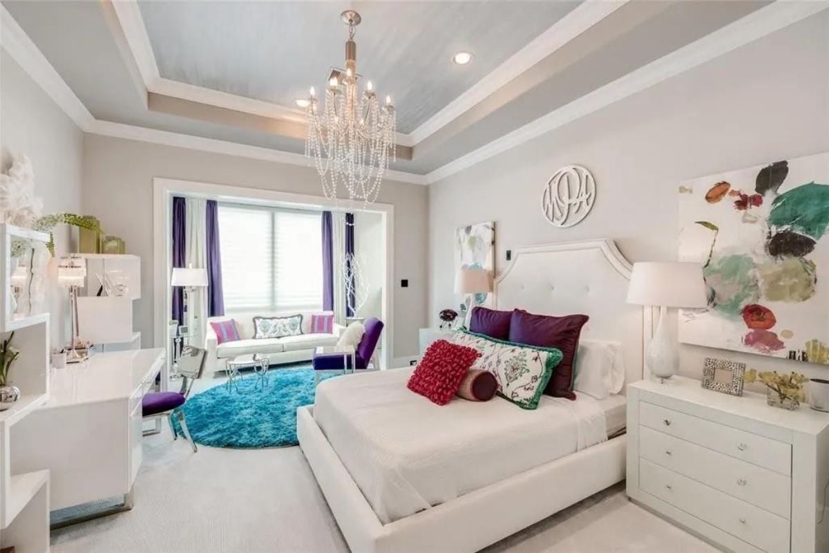 A bedroom with a bed, chandelier, cabinets, rug, couch, and painting.