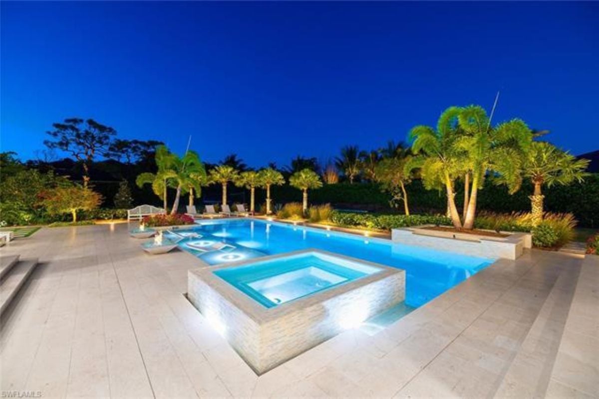 A swimming pool with a jacuzzi surrounded by plants and trees.