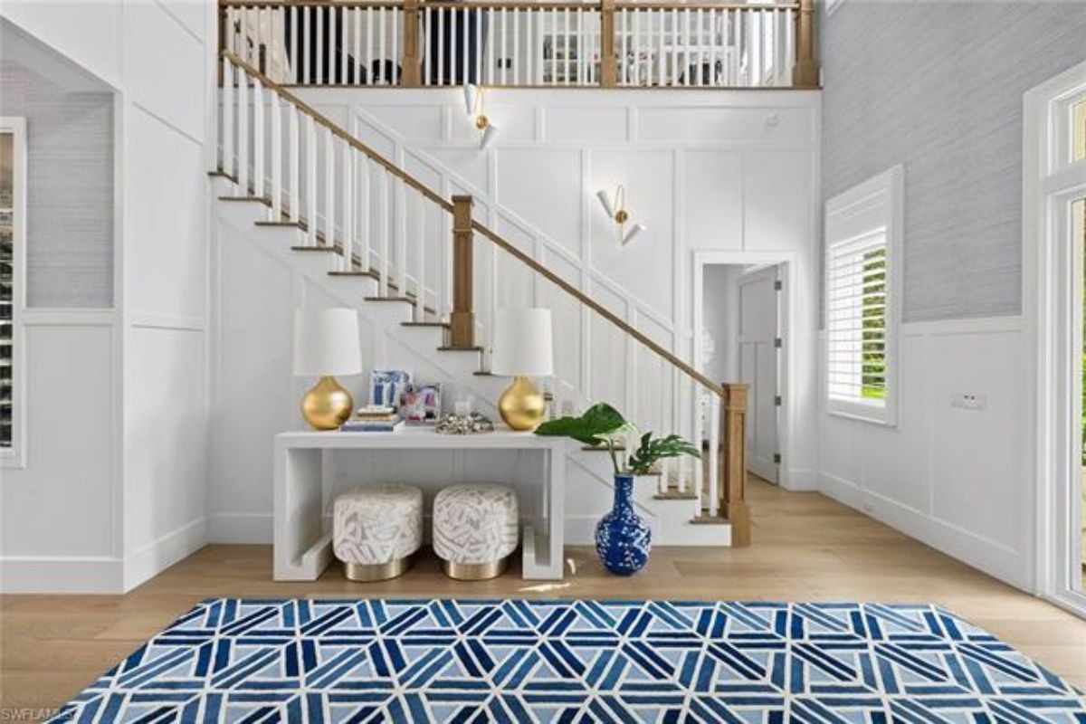 A foyer with a table, vase, lampshades, rug, and staircase.