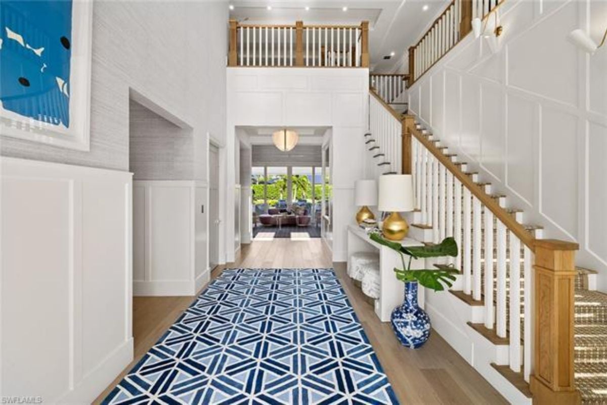 A foyer with a table, vase, lampshades, rug, and staircase.