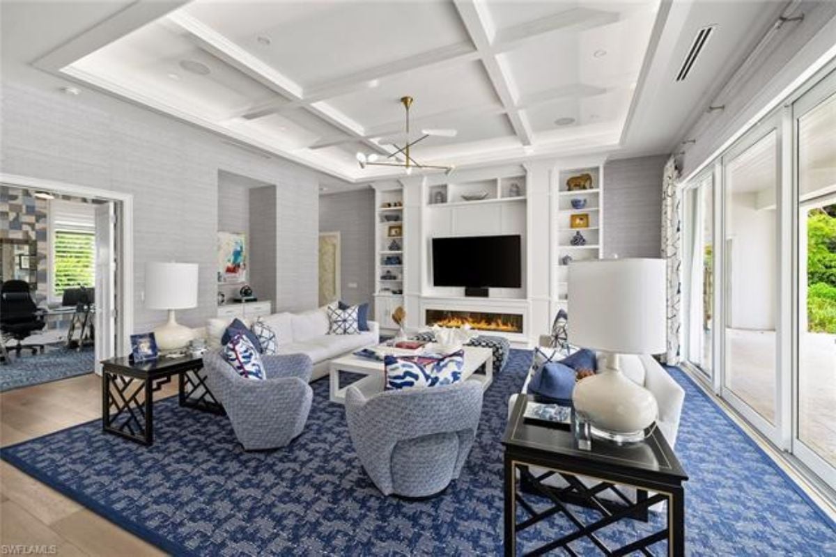 A living room with a rug, white couches, chairs, a center table, TV, fireplace, and shelves.