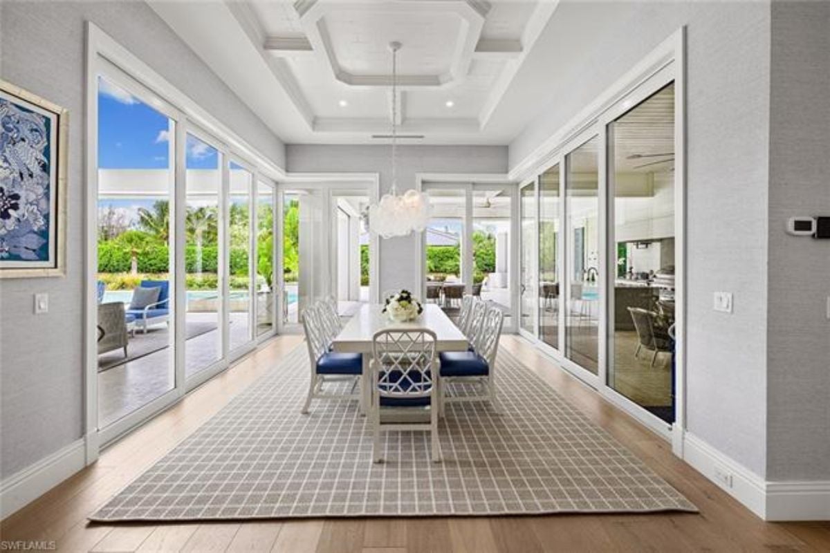 A dining room with glass walls, a rug, and a dining table surrounded by chairs.