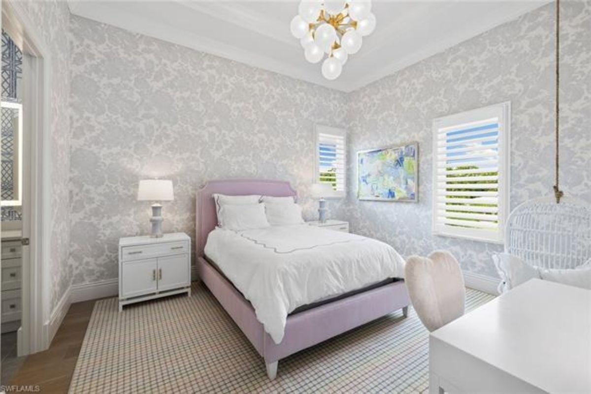 A bedroom with a bed, wallpaper, chandelier, windows, and nightstands.