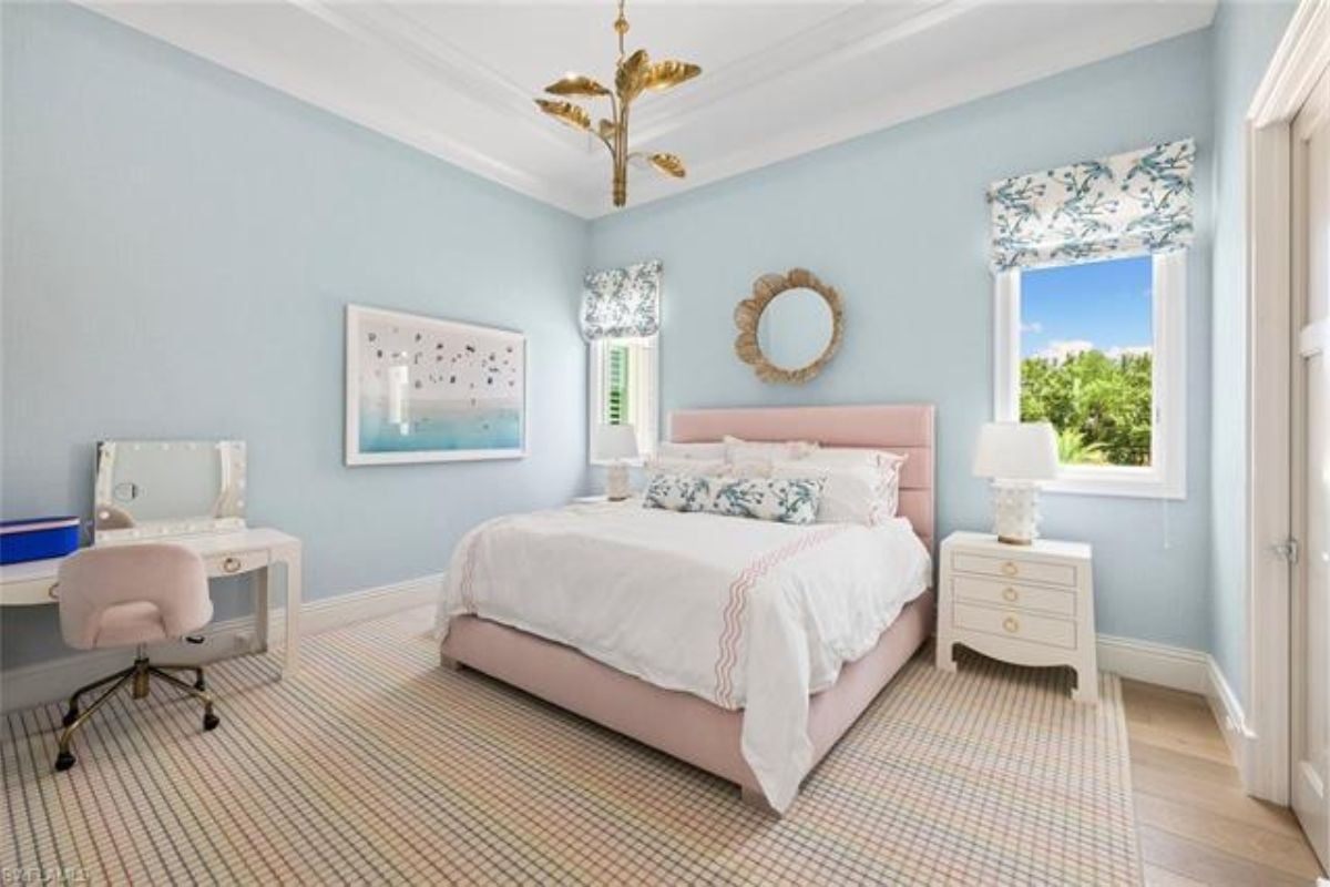 A bedroom with a bed, windows, a nightstand, a rug, a desk, and a chair.