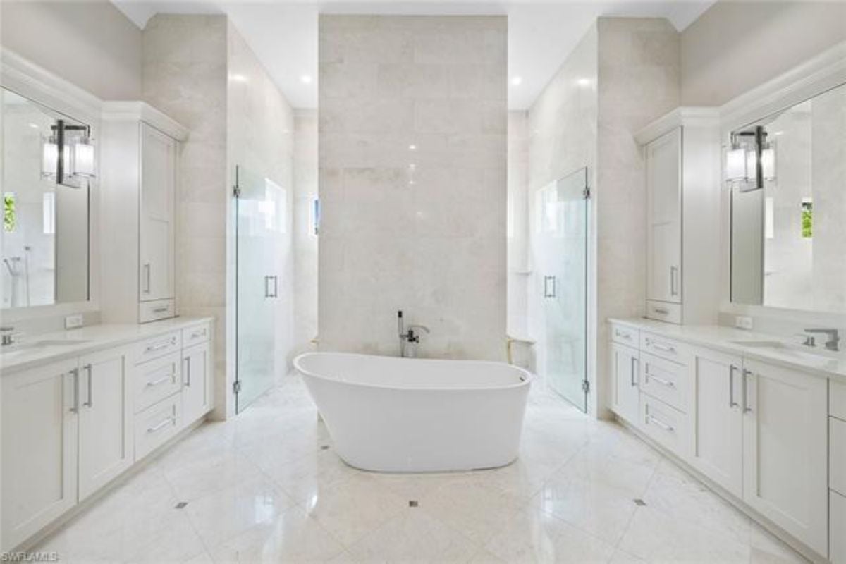 A bathroom with tiled floors, vanities, mirrors, cabinets, and a bathtub.