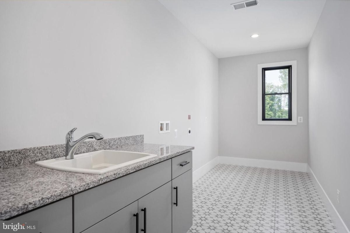 A bathroom with a window, tiled floor, vanity, and cabinets.