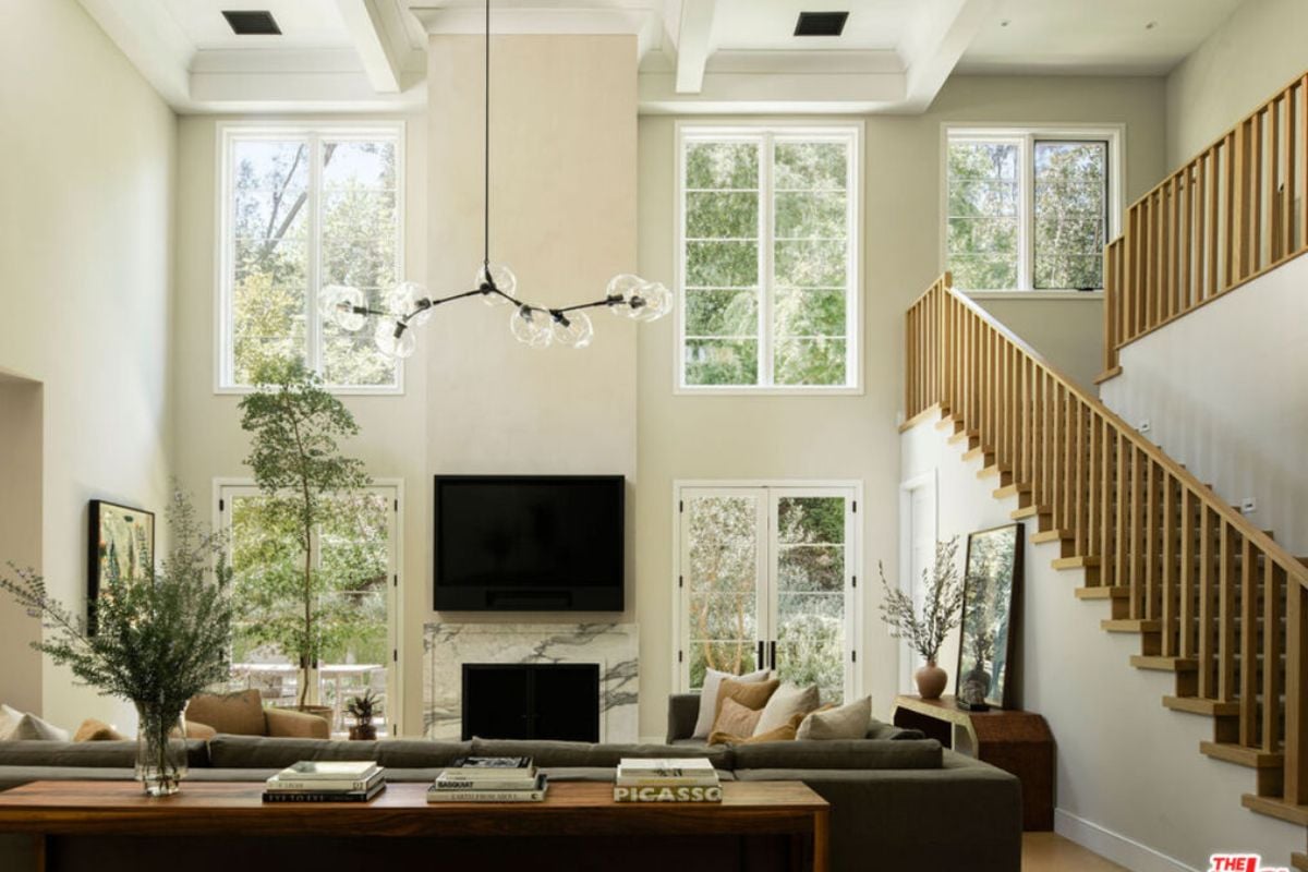 A family room with windows, a TV, a fireplace, a chandelier, and couches.