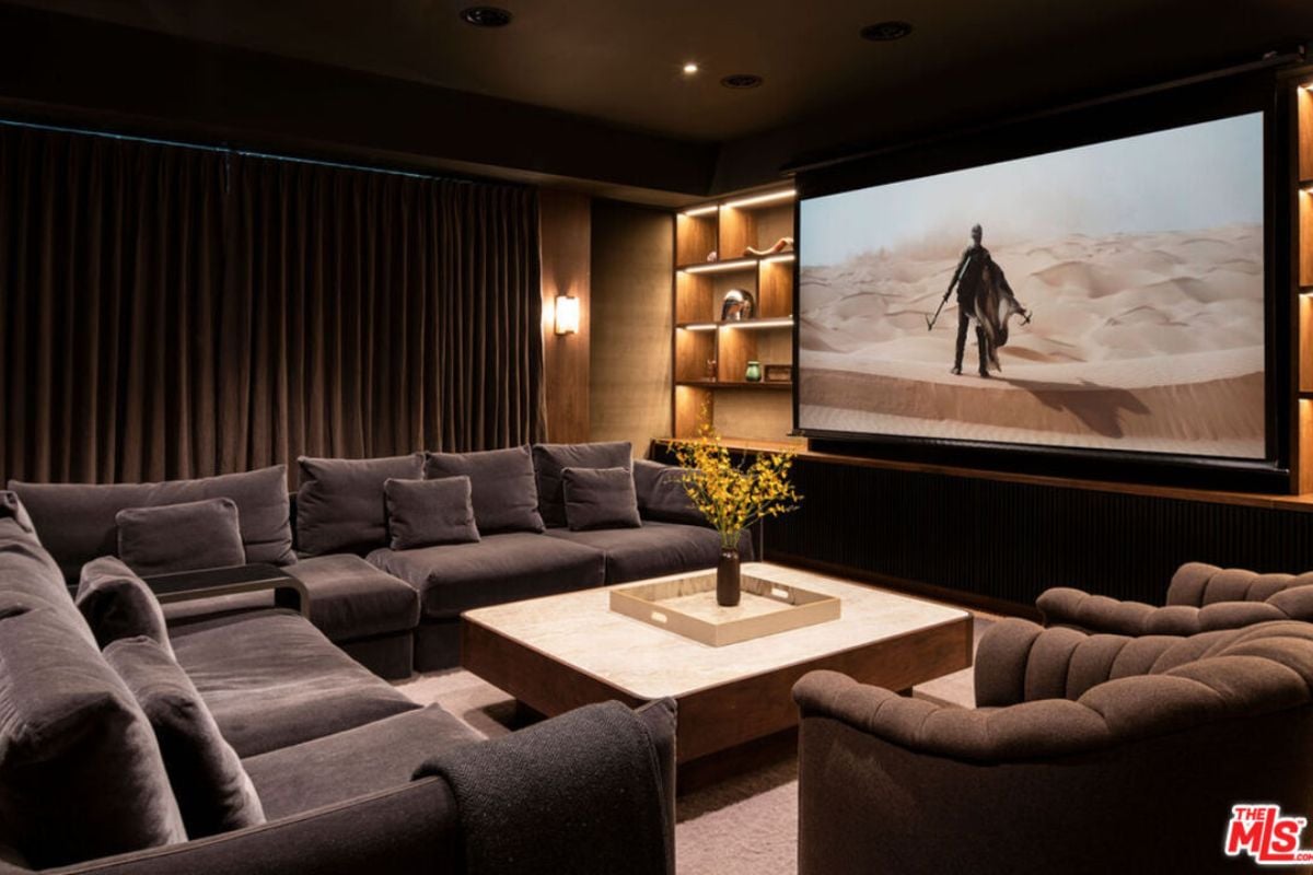 A home theater with a large screen, shelves, curtains, black couches, and a center table.
