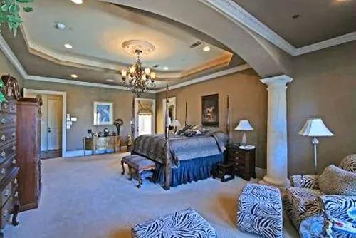 Primary suite with a tray ceiling, a four-poster bed, and a sitting area separated by an archway.