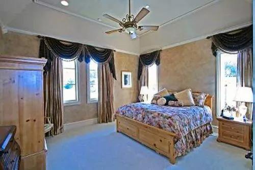 Bedroom with light wood furnishings and white-framed windows dressed in flowy curtains and valances.