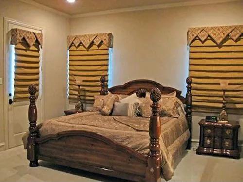 Bedroom with a four-poster bed and windows covered in roman shades.