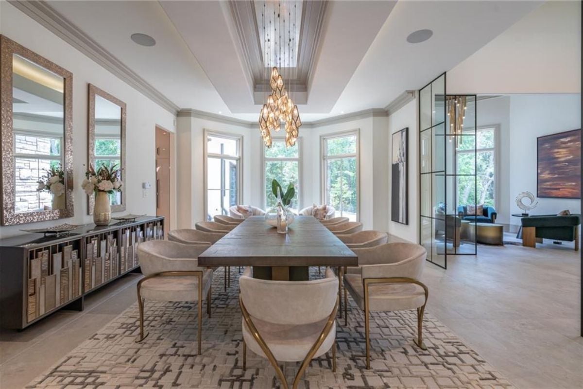 A dining room with a chandelier, a mirror, a cabinet, a rug, and a long dining table.