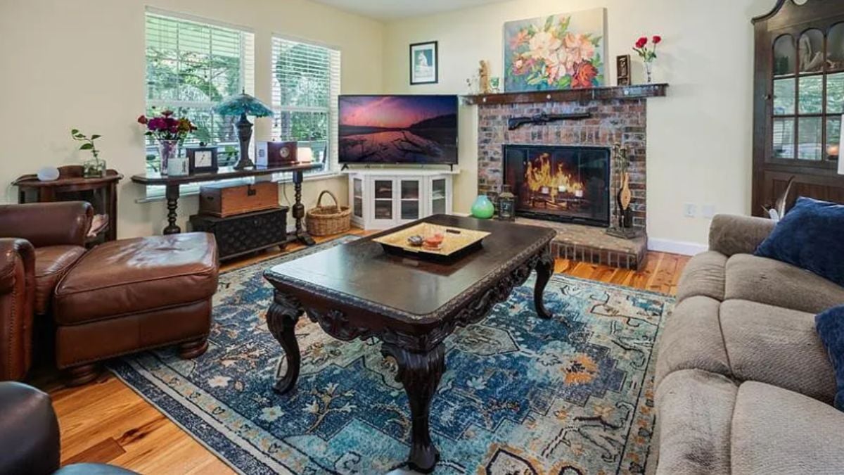 A living room with a window, fireplace, TV, paintings, a cabinet, a rug, a couch, and a center table.