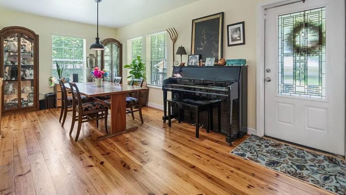 A dining room with windows, a painting, and a dining table surrounded by chairs.