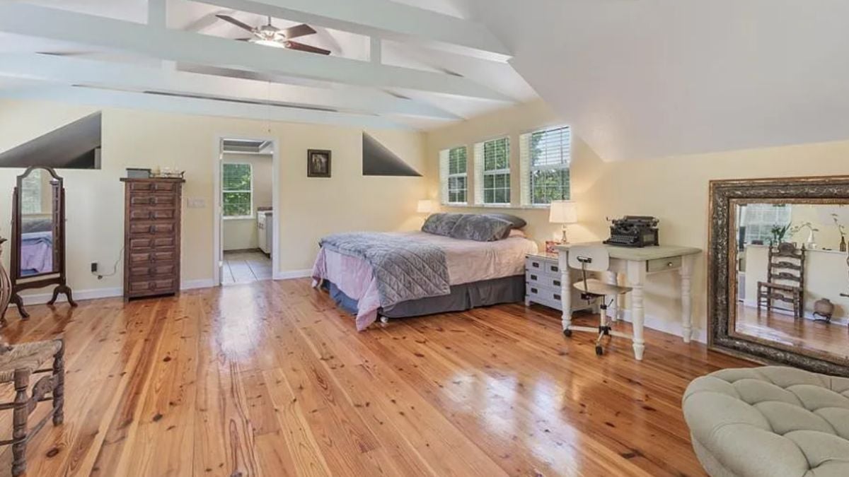 A bedroom with a bed, ceiling fan, exposed beam ceiling, windows, mirrors, a cabinet, a nightstand, and a desk with a chair.