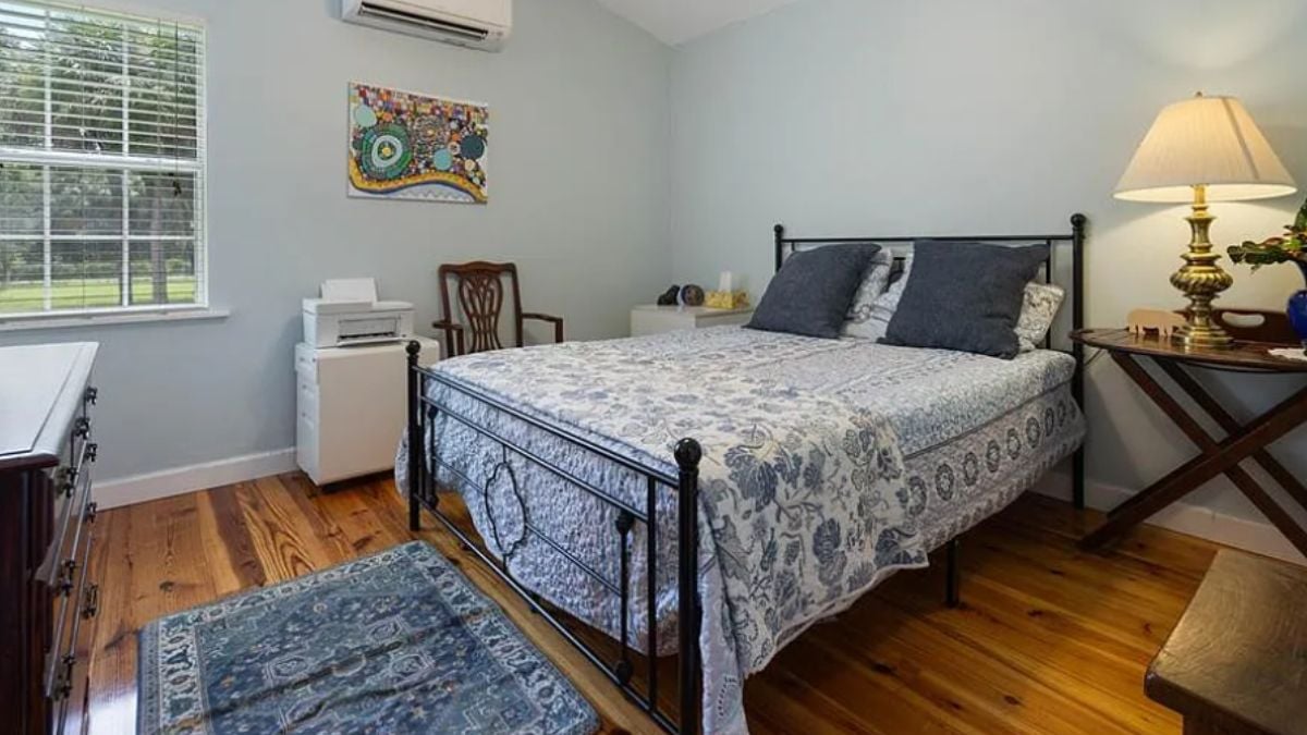 A bedroom with a bed, a window, a side table, a rug, and a cabinet.