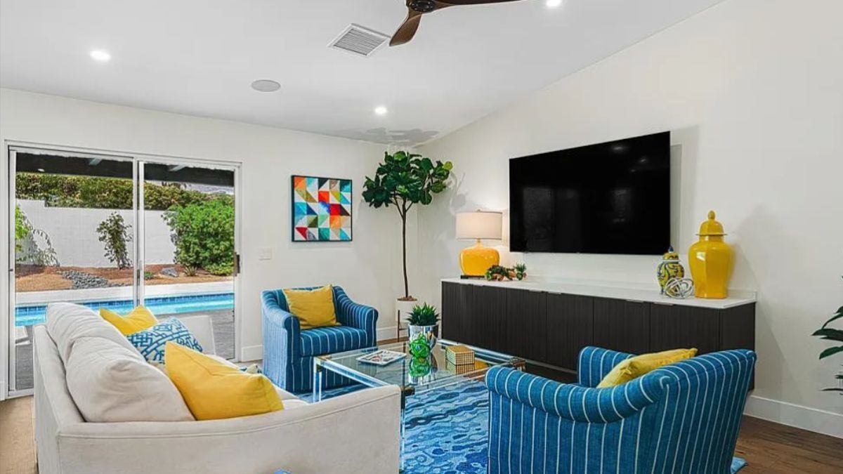 A living room with a ceiling fan, a window, a TV, a cabinet, a rug, couches, and a glass coffee table.