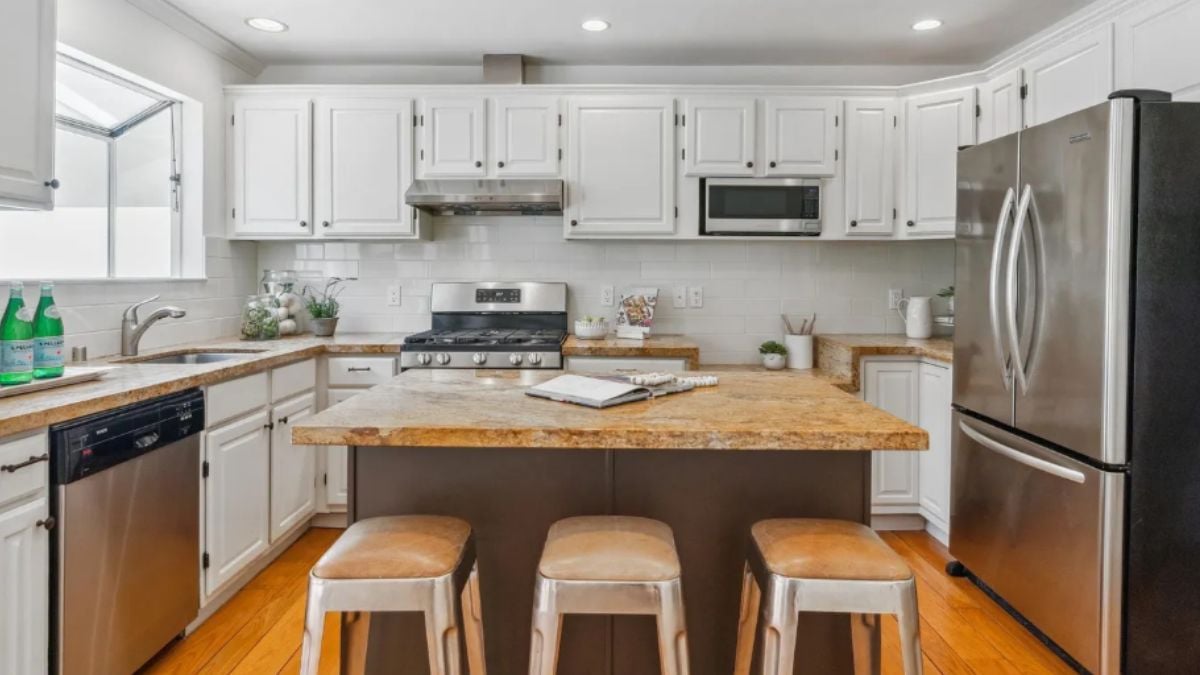 A kitchen with a center island, chairs, countertops, cabinets, and kitchen appliances.