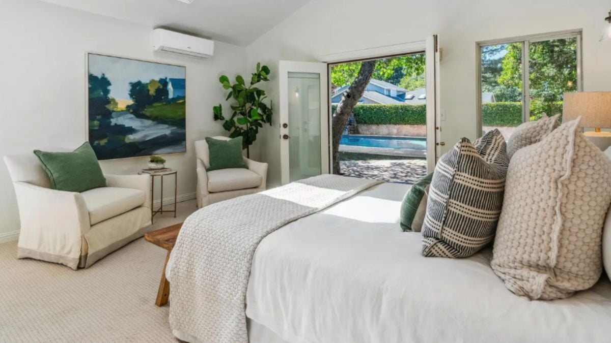 A bedroom with a bed, window, painting, houseplant, and chairs.