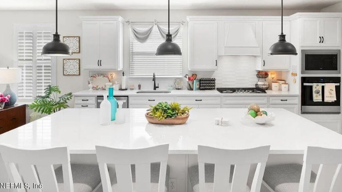 A kitchen with an island, chairs, countertops, a sink, cabinets, and kitchen appliances.