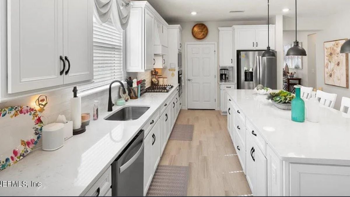 A kitchen with an island, chairs, countertops, a sink, cabinets, and kitchen appliances.