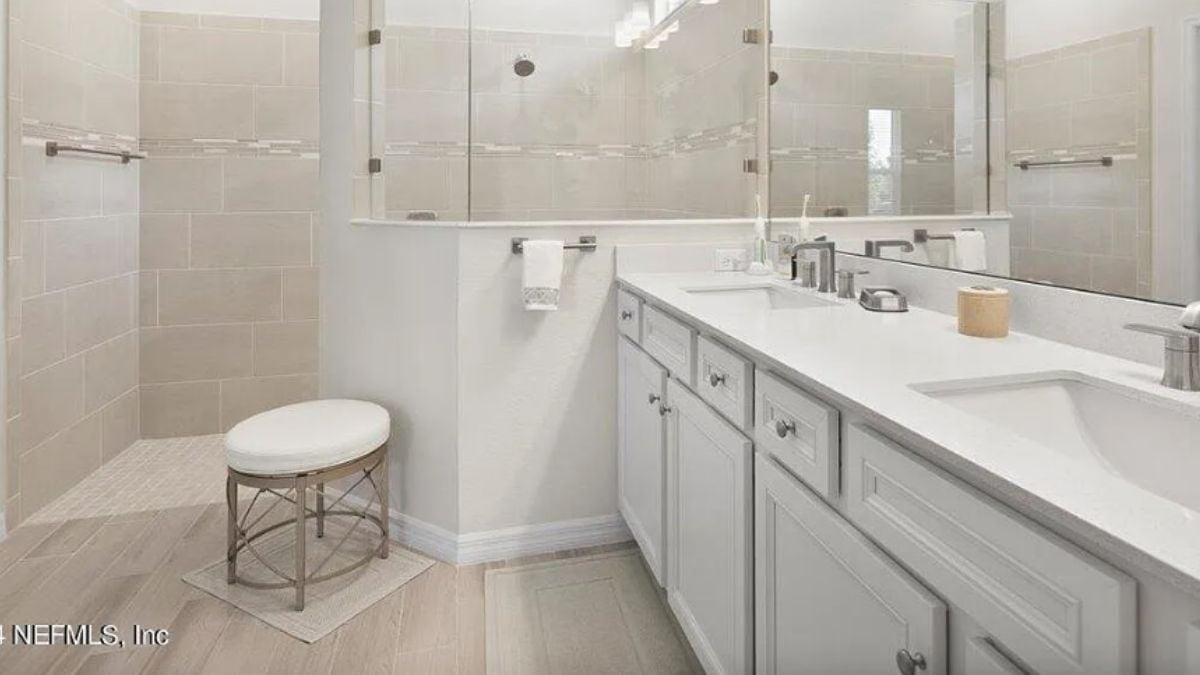 A bathroom with a vanity, cabinets, a mirror, and a shower.