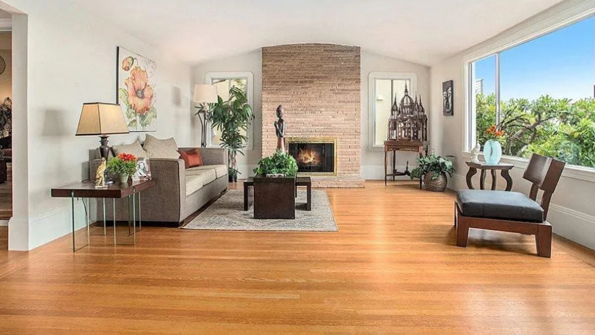 A living room with a fireplace, window, painting, chair, houseplant, and center table.