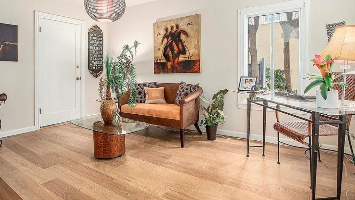A home office with a painting, windows, a couch, a center table, and a desk with a chair.
