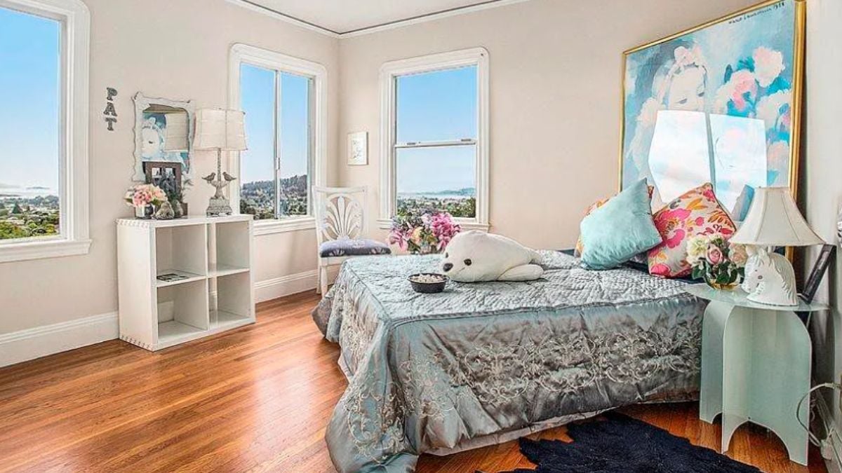 A bedroom with a bed, windows, paintings, and a nightstand.